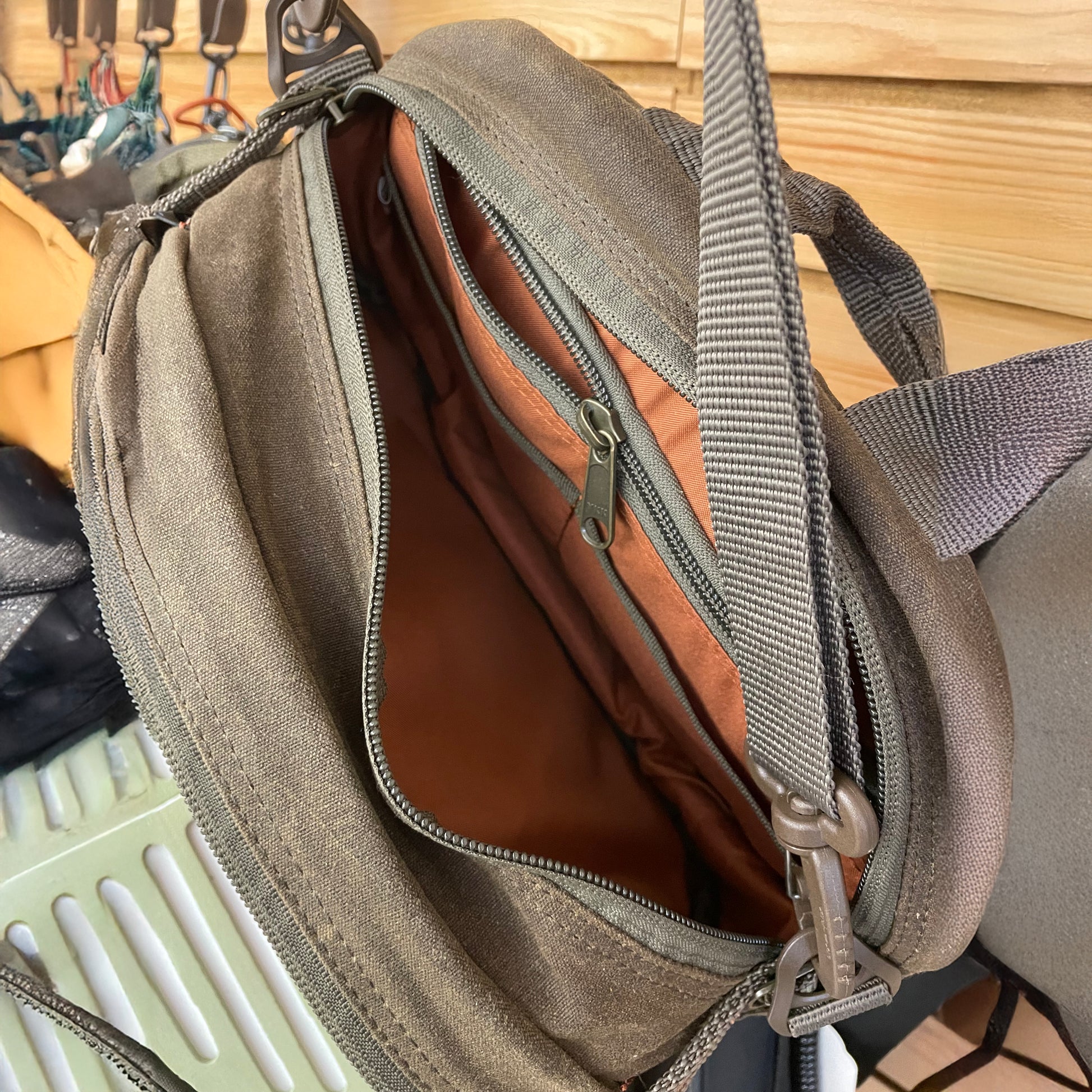 Fishpond Blue River Chest/ Lumbar Pack shown hanging from the chest strap with the main zippered compartment open showing an internal zippered compartment and two accessory pockets 